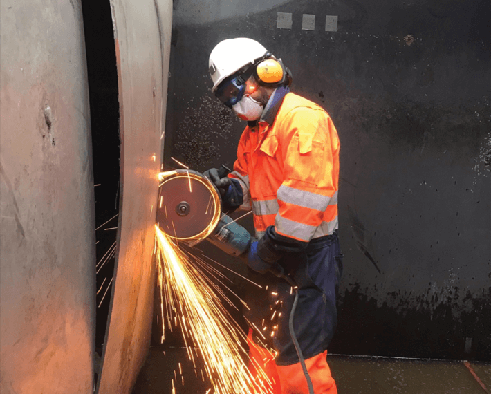 Man in PPE with a metal saw cutting through metal, with sparks flying out