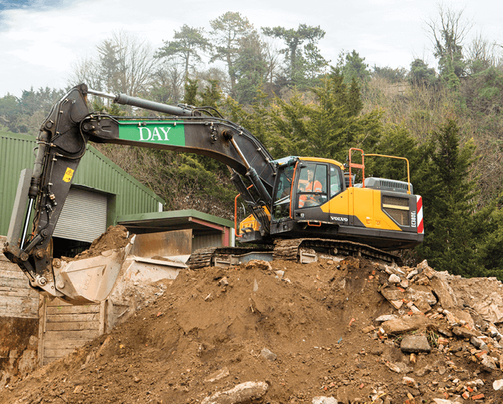 Yellow excavator on top of a pile of rubble with a green Day Tag on the arm