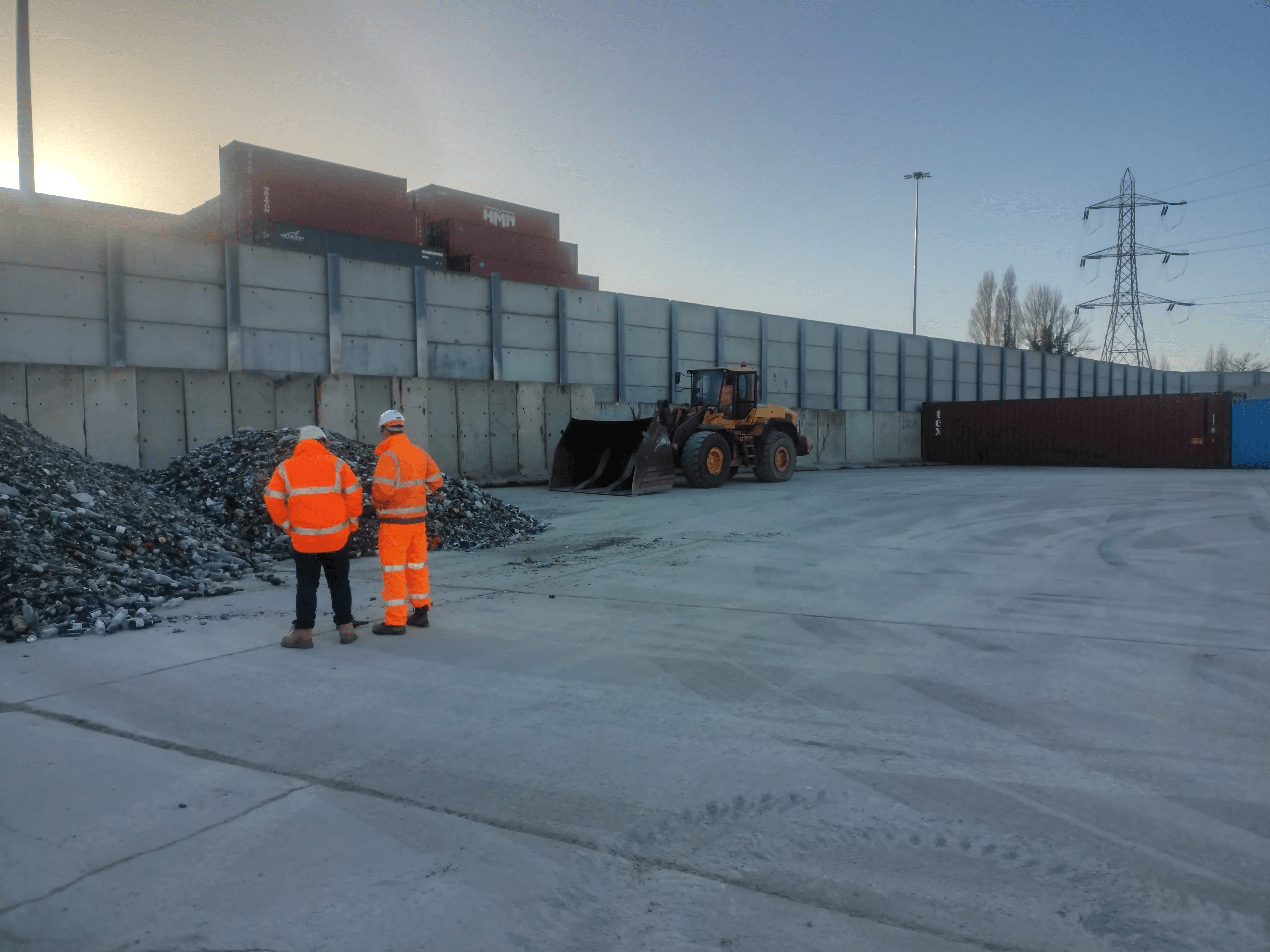 two workers in PPE standing over a pile of recycled glass